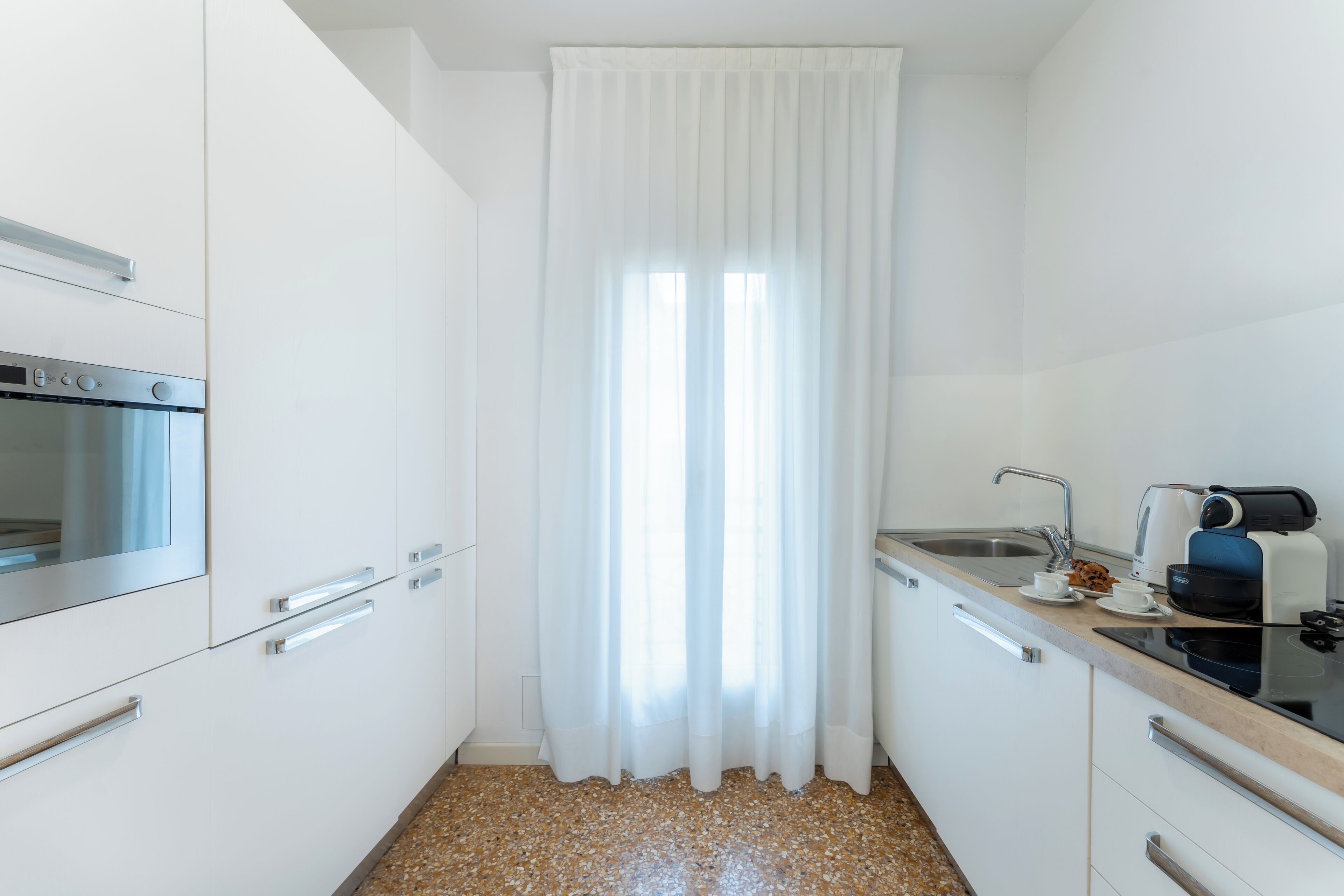 A modern kitchen with white cabinets, a stainless steel oven, a coffee maker, and a sink.