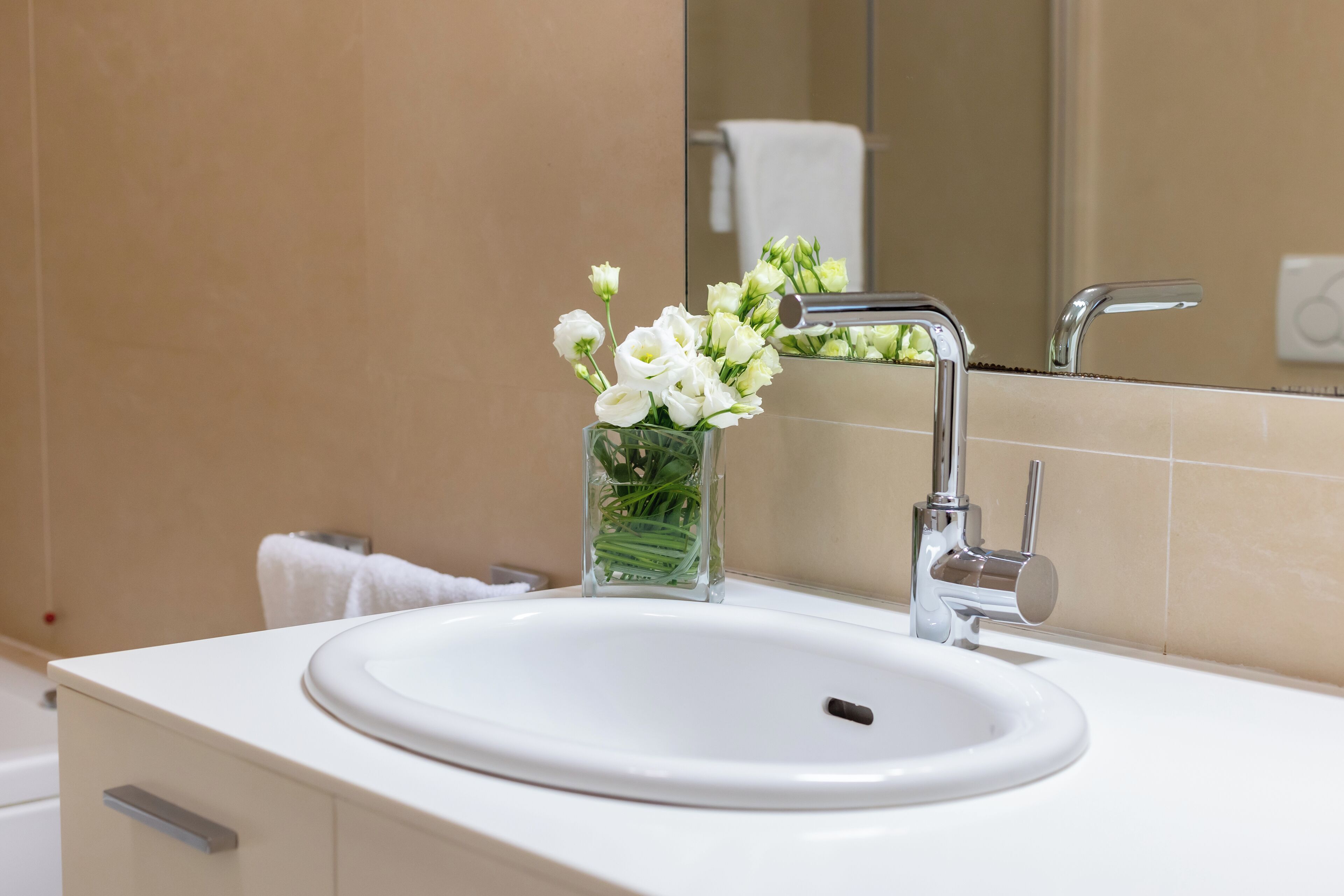 A bathroom with a white sink, a mirror, and a glass vase with white flowers.