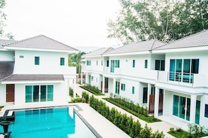 Un resort moderno con piscina, edificios blancos y jardines verdes.