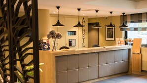 A reception desk with a cushioned backrest, pendant lighting, and a wooden panel design. - Brit Hotel Le Lodge (Strasbourg)