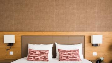 A hotel room with a wooden headboard, two bedside lamps, a bed with white bedding, and two patterned pillows.