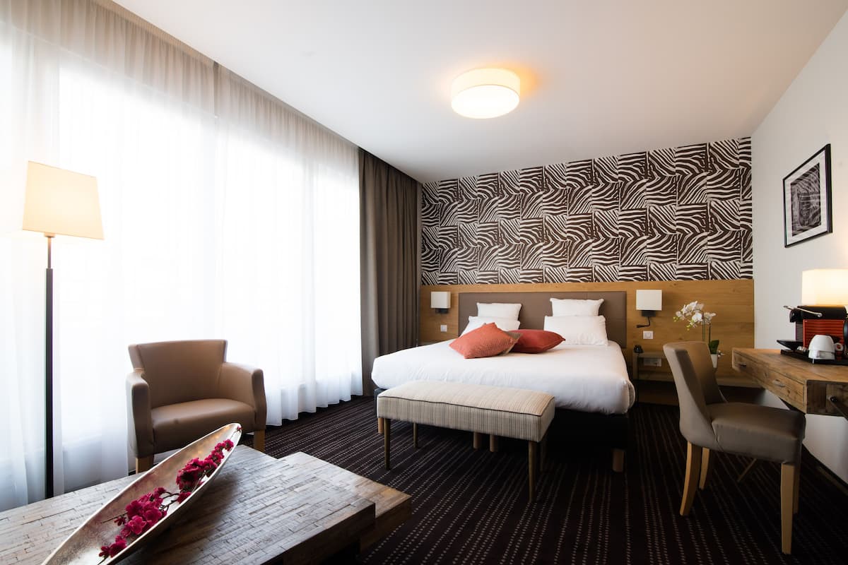 Ein Hotelzimmer mit einem Bett, einem Schreibtisch, einem Sessel und einem Fenster mit Vorhängen.