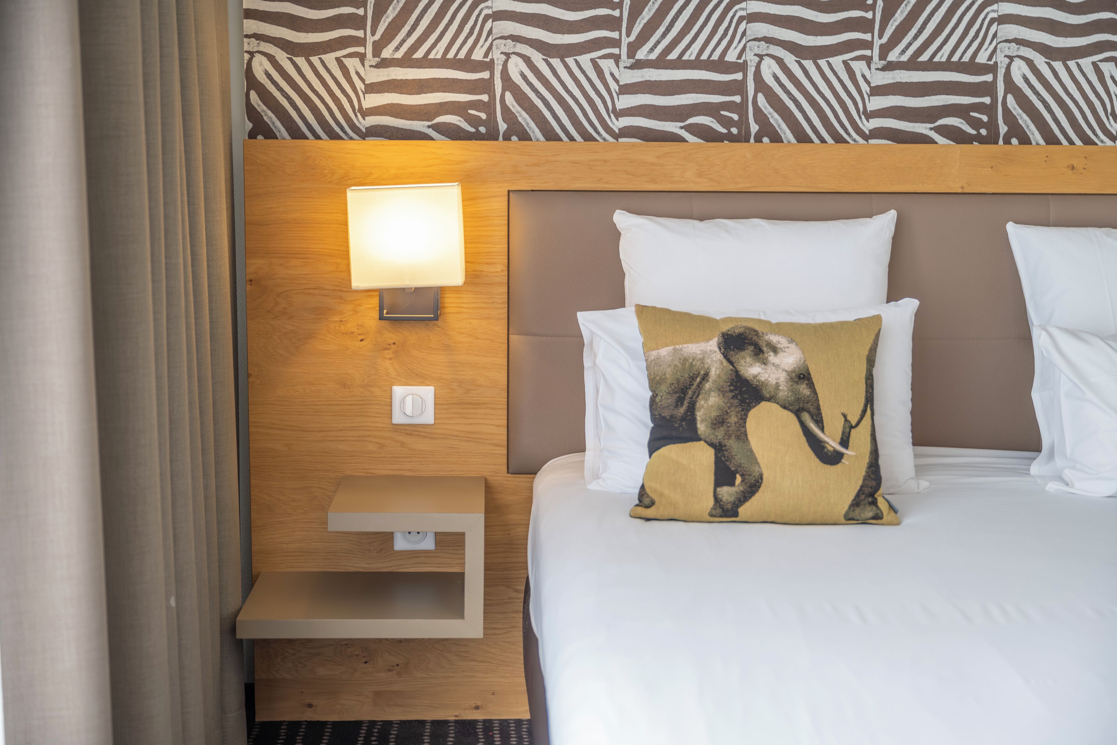 Ein Hotelzimmer mit einem Bett, einem Nachttisch mit Lampe und einer Wand mit Zebramuster.