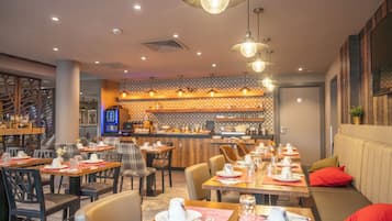 Un restaurante con varias mesas y sillas, una zona de bar y un área de estar con un sofá y cojines rojos.