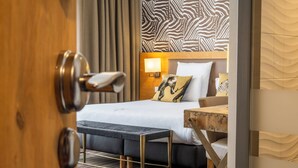 A hotel room with a bed, bench, and a wooden side table. - Brit Hotel Le Lodge (Strasbourg)