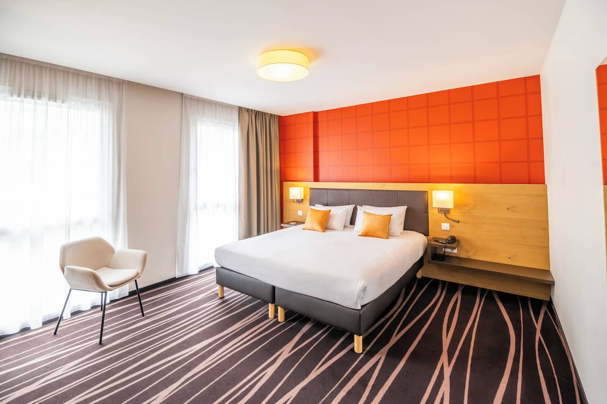 Ein Hotelzimmer mit einem großen Bett, einem Sessel, einem Nachttisch und einer Wand mit Gittermuster.