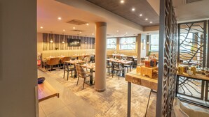 A modern restaurant with a mix of booth and table seating, a central column, and a decorative wall with a tree-like pattern. - Brit Hotel Le Lodge (Strasbourg)