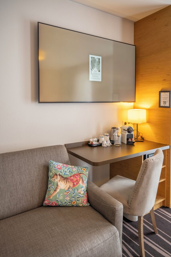 Habitación de hotel con sofá, una silla, escritorio con lámpara y un cartel en la pared.