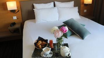 Een keurig opgemaakt hotelbed met witte lakens, een dienblad met croissants, een kop koffie, een vaas met bloemen en een theepot.