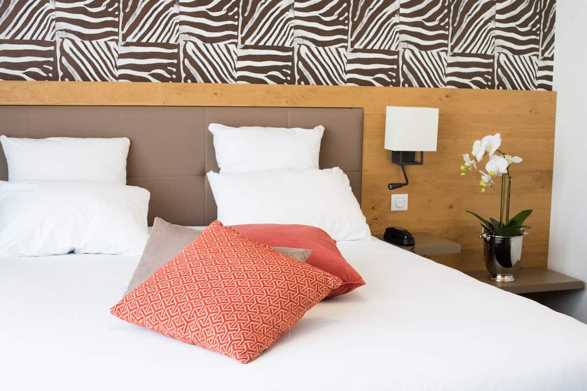 Ein Hotelzimmer mit einem hölzernen Kopfende, weißer Bettwäsche und einem gemusterten Kissen.