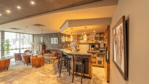 A modern kitchen with a bar area, wooden furniture, and a large window. - Brit Hotel Le Lodge (Strasbourg)
