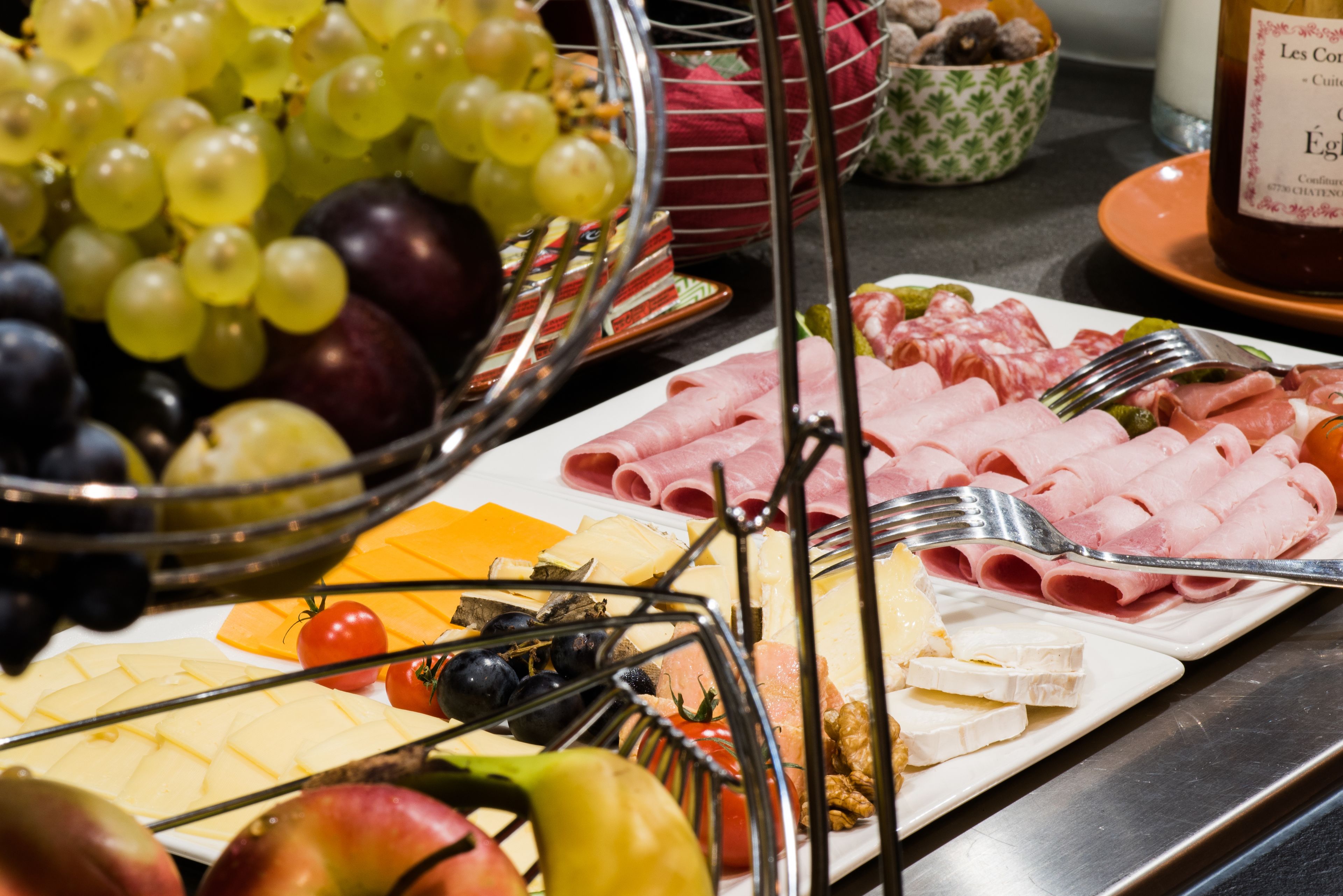 A buffet with various cheeses, meats, fruits, and vegetables.