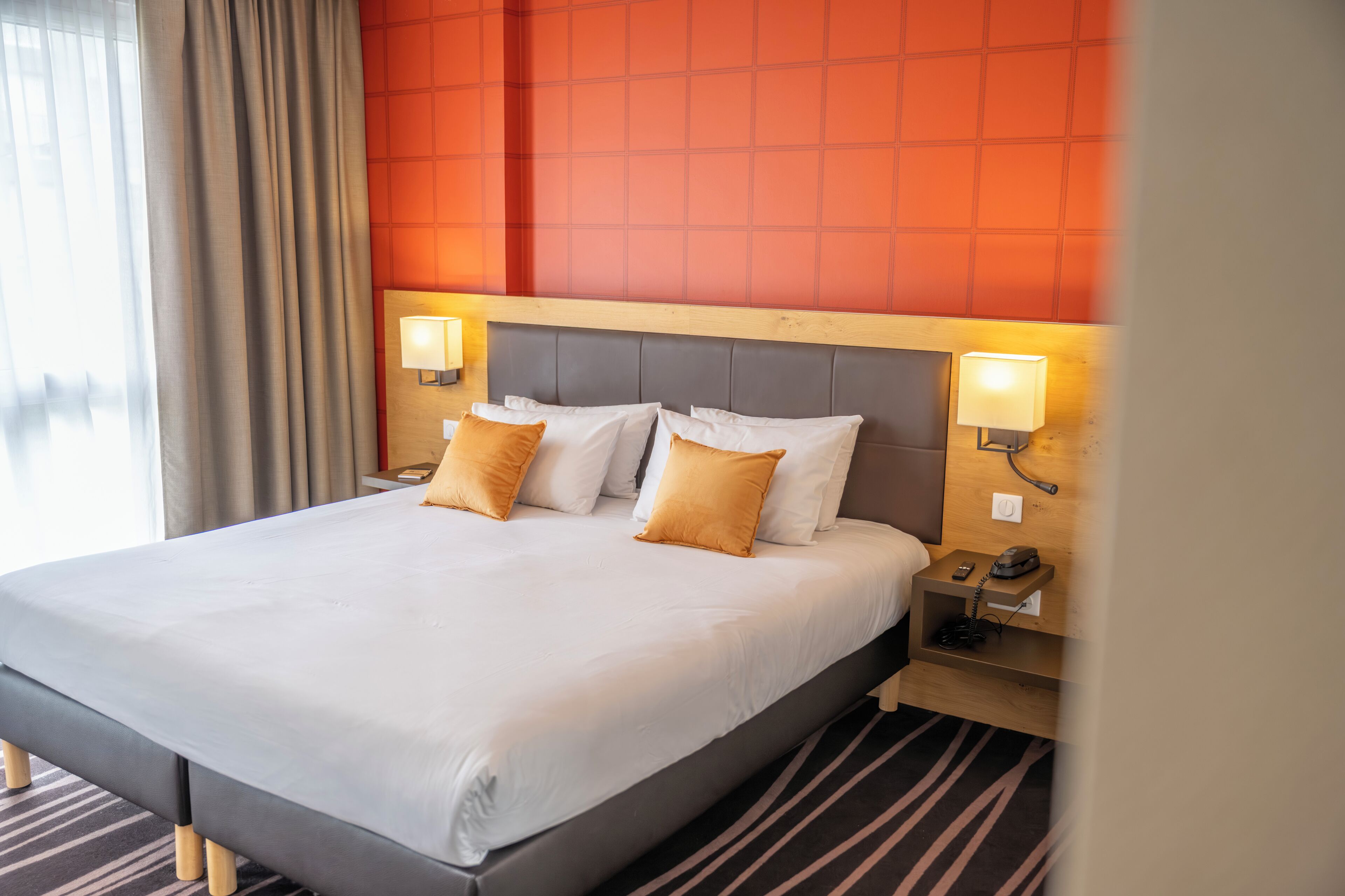 A hotel room with a large bed, two bedside lamps, a wooden nightstand, and a view of the outdoors.