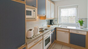 Eine Küche mit Mikrowelle, Herd, Backofen und Spüle. Ein Fenster mit Vorhang und eine Pflanze stehen auf der Arbeitsfläche.