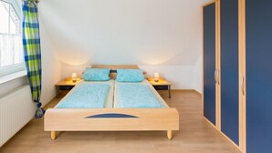 Ein Schlafzimmer mit einem hölzernen Bett, zwei Nachttischen mit Lampen, einem Kleiderschrank und einem Fenster mit Vorhängen.