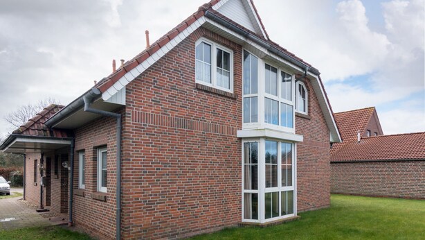 Ein zweigeschossiges Backsteinhaus mit geneigtem Dach, einer Veranda und einem großen Erkerfenster.