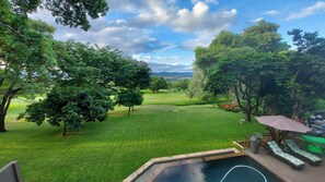 A backyard with a swimming pool, a grassy lawn, and a view of a golf course. - Matumi Golf Lodge (Mbombela)