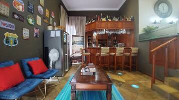 A living room with a blue sofa, a wooden coffee table, and a bar area with stools and a wine rack.