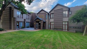 Um hotel moderno com entrada central, várias janelas e um gramado bem cuidado.