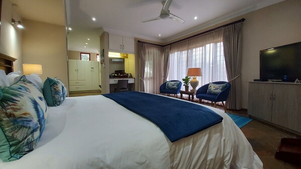 Una habitación de hotel con una cama grande, un escritorio, una silla, un televisor y un ventilador de techo.