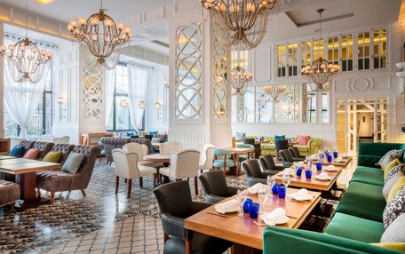 A spacious hotel lobby with multiple seating areas, elegant chandeliers, and large windows.