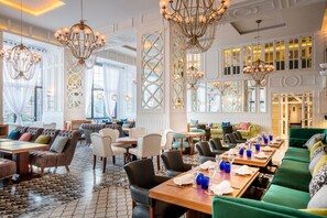 En rymlig hotellobby med flera sittgrupper, eleganta kristallkronor och stora fönster.