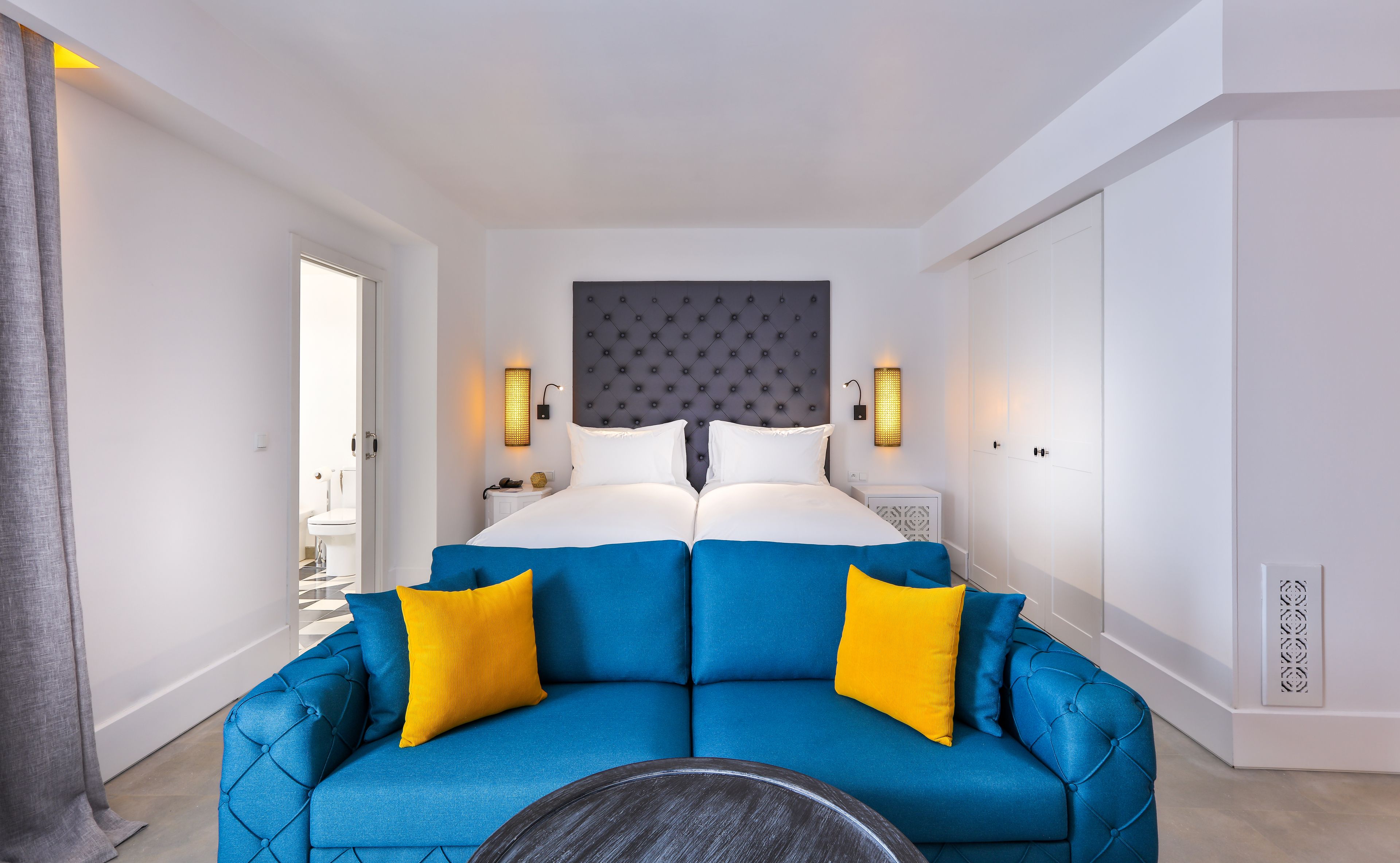 Ein modernes Hotelzimmer mit einem großen Bett, einem blauen Sofa mit gelben Kissen und einem runden Tisch.