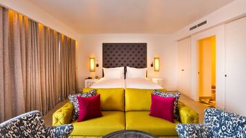 Habitación de hotel con una cama grande, un sofá, dos sillones, una mesita de noche y una lámpara de pared.