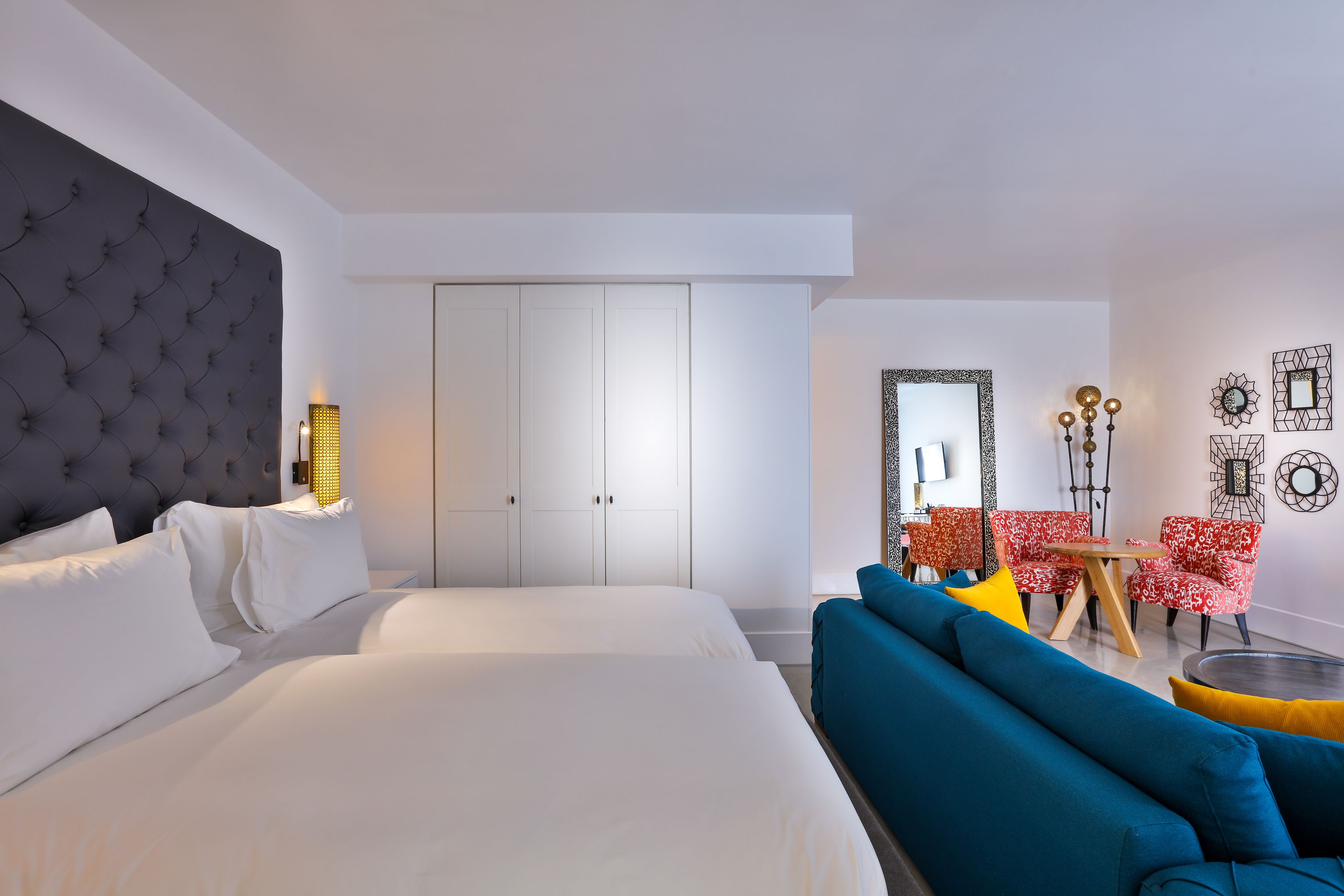 A modern hotel room with a large bed, a sofa, a dining table, and a seating area with red and white patterned chairs.