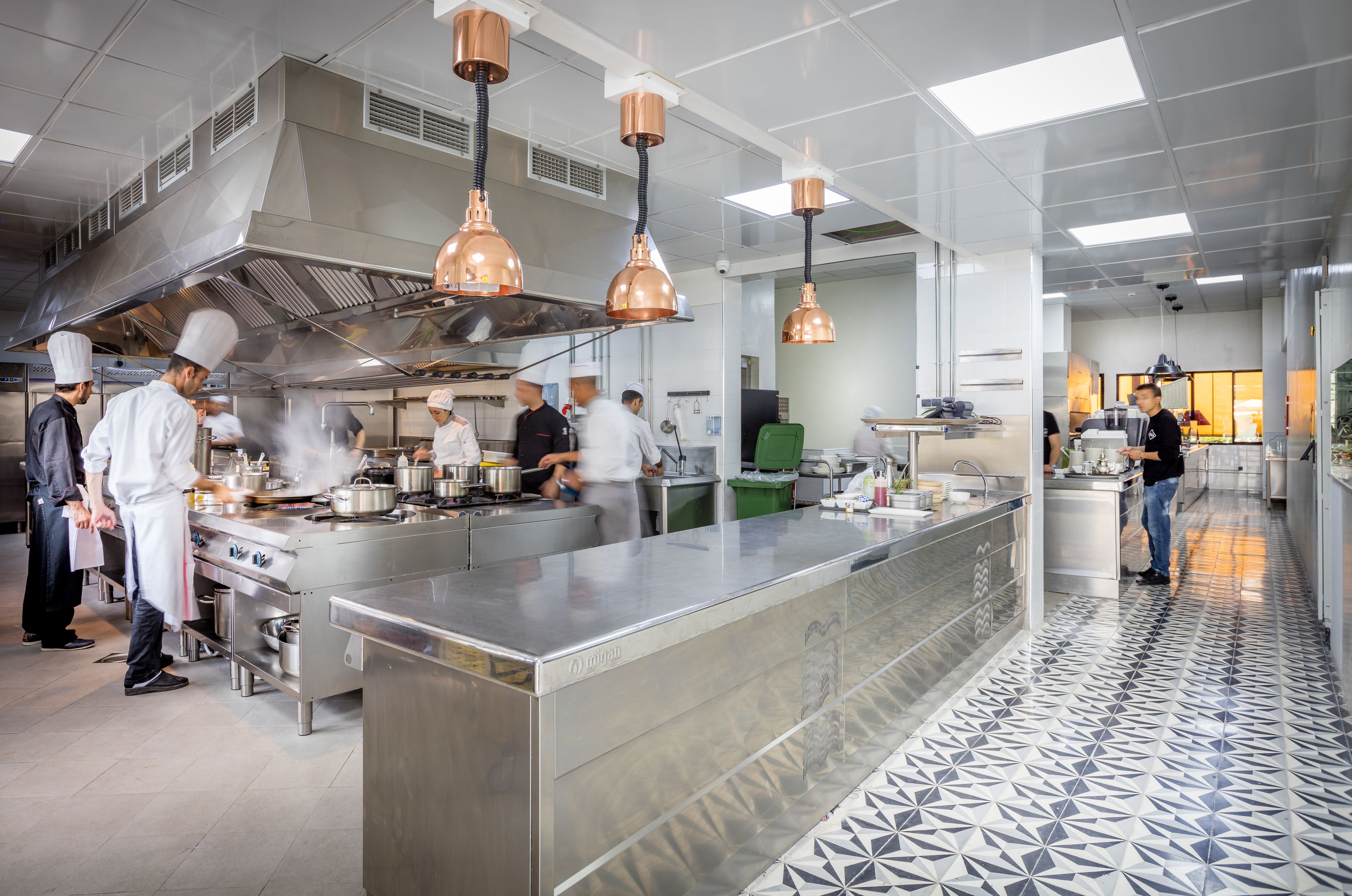 A modern kitchen with stainless steel appliances, copper pendant lights, and a patterned floor.