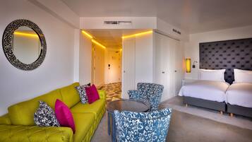 Una habitación de hotel con un sofá verde, sillones estampados, una cama y un espejo grande.