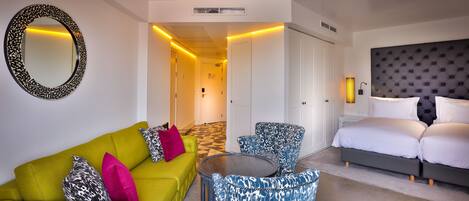 A hotel room with a green sofa, patterned armchairs, a bed, and a large mirror.