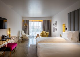 Habitación de hotel con una cama grande, un escritorio con computadora, una silla, una mesita y un televisor.