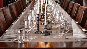 Uma longa mesa de jantar posta com velas, copos e uma toalha de mesa estampada.