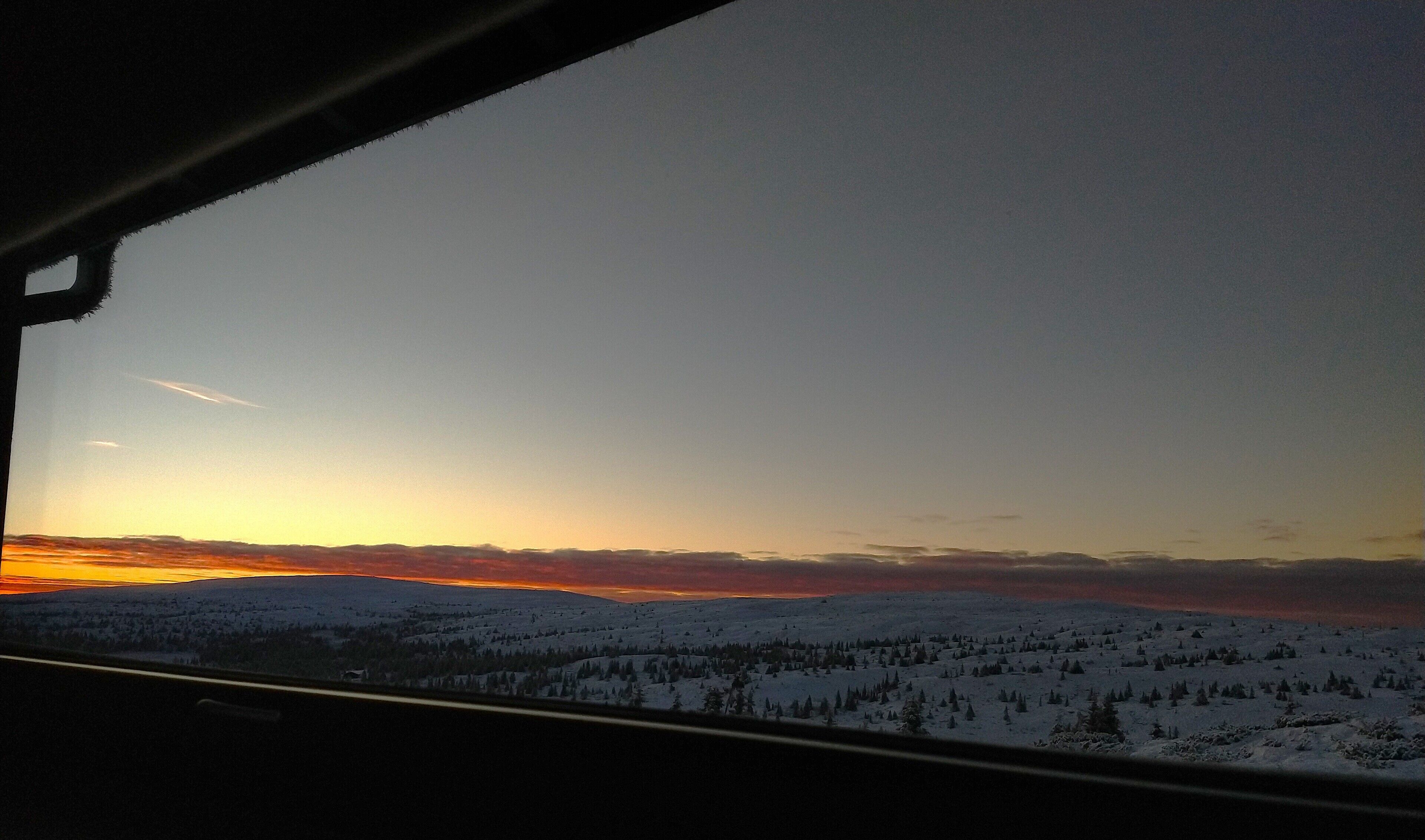 A view from inside a vehicle, looking out at a snowy landscape during sunset.