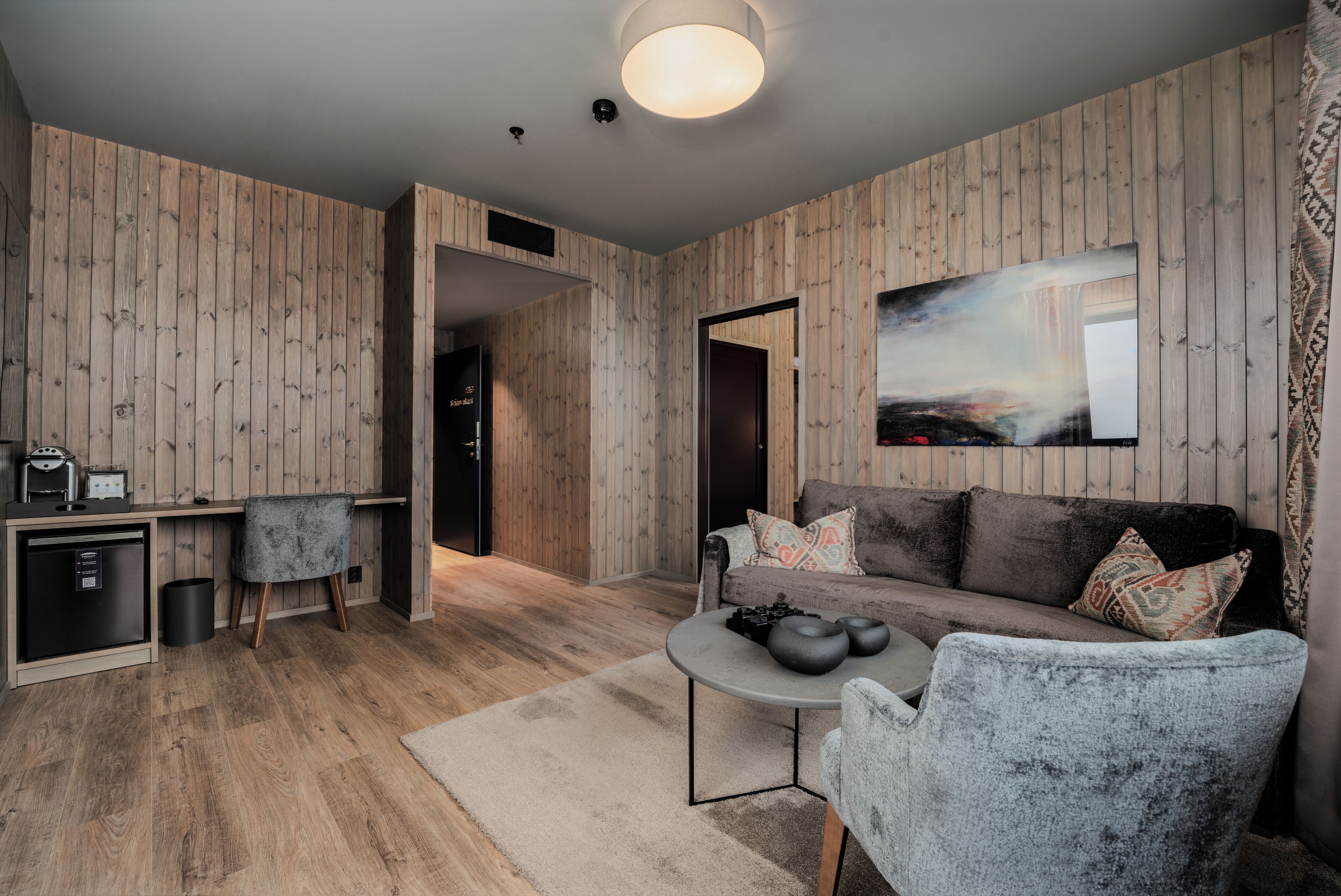 Een moderne woonkamer met houten lambrisering, een grijze bank, een salontafel en een aan de muur bevestigde televisie.