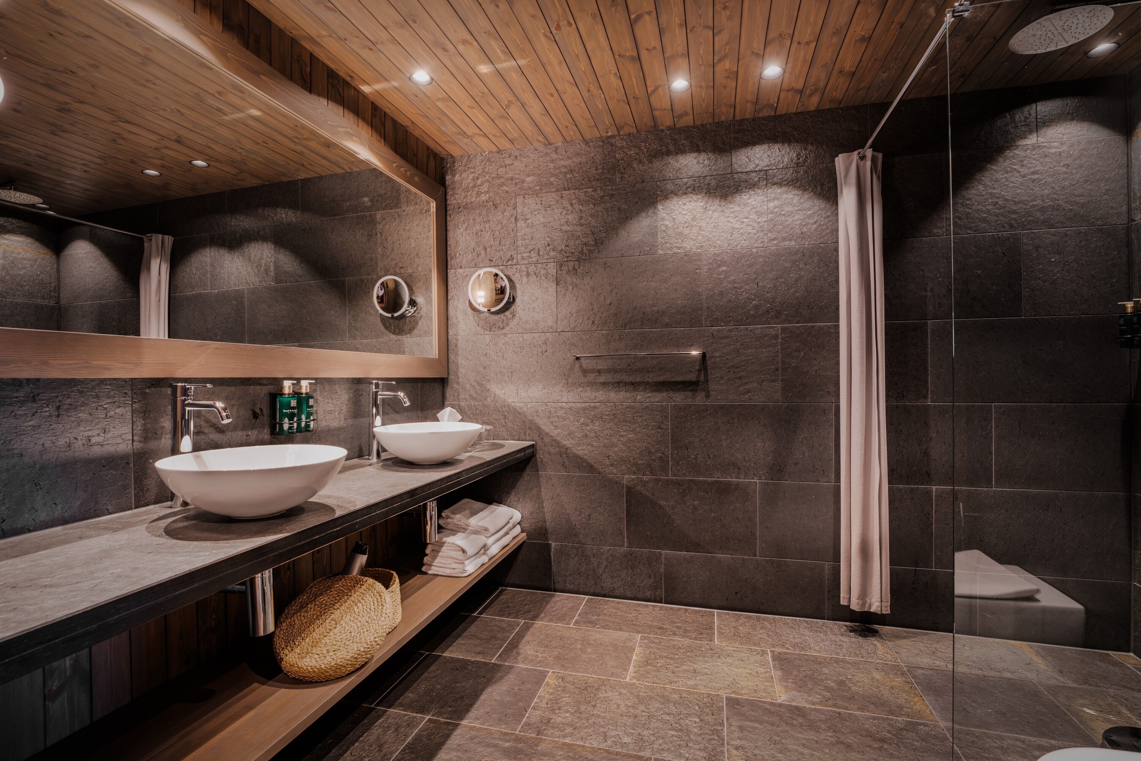 A modern bathroom with a wooden ceiling, two sinks, a shower, and a large mirror.