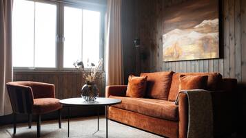 A cozy living room with a wooden wall, a large window, a brown sofa, a round coffee table, and a chair.