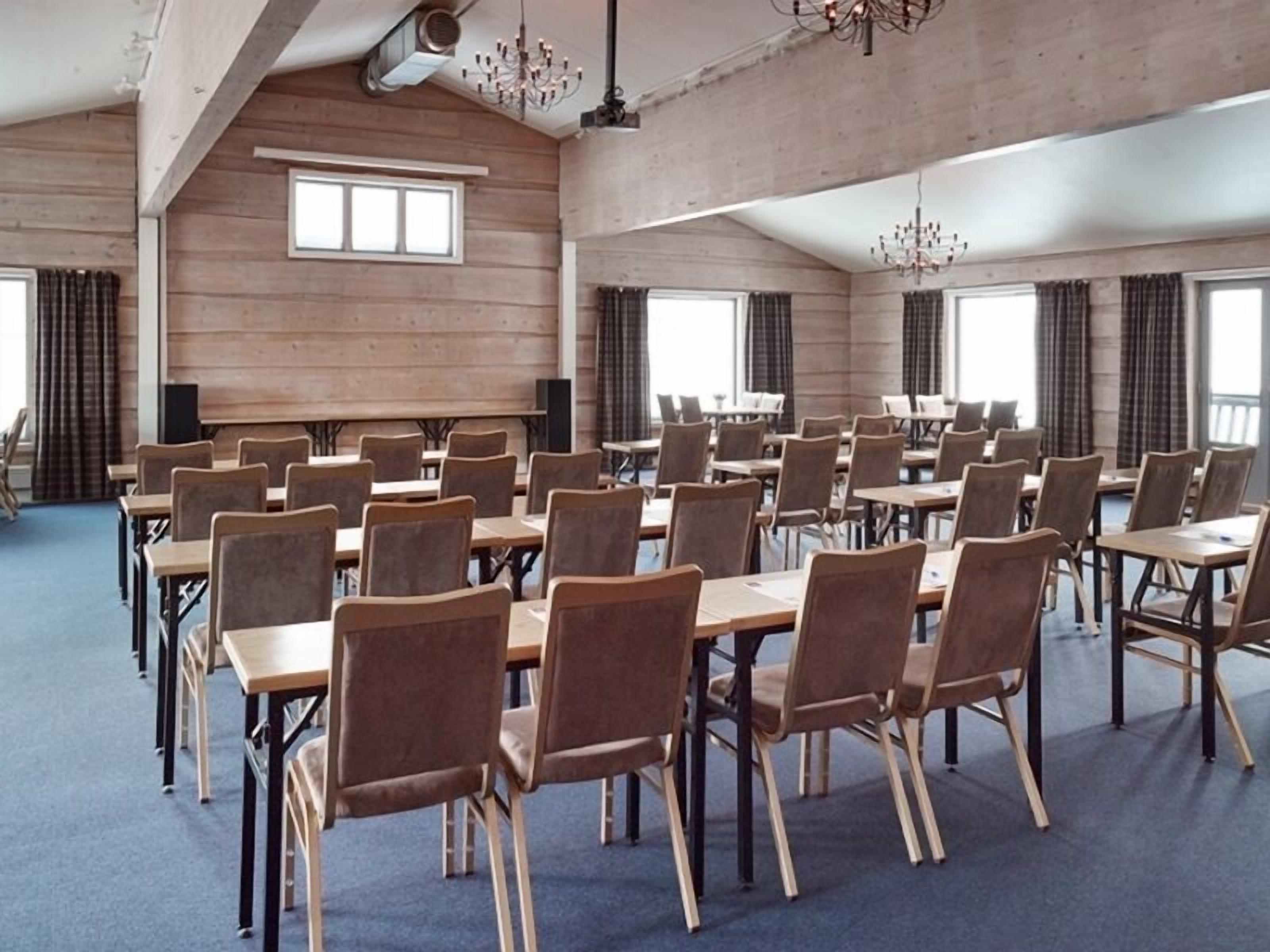 A conference room with rows of tables and chairs, large windows, and a high ceiling with exposed beams.