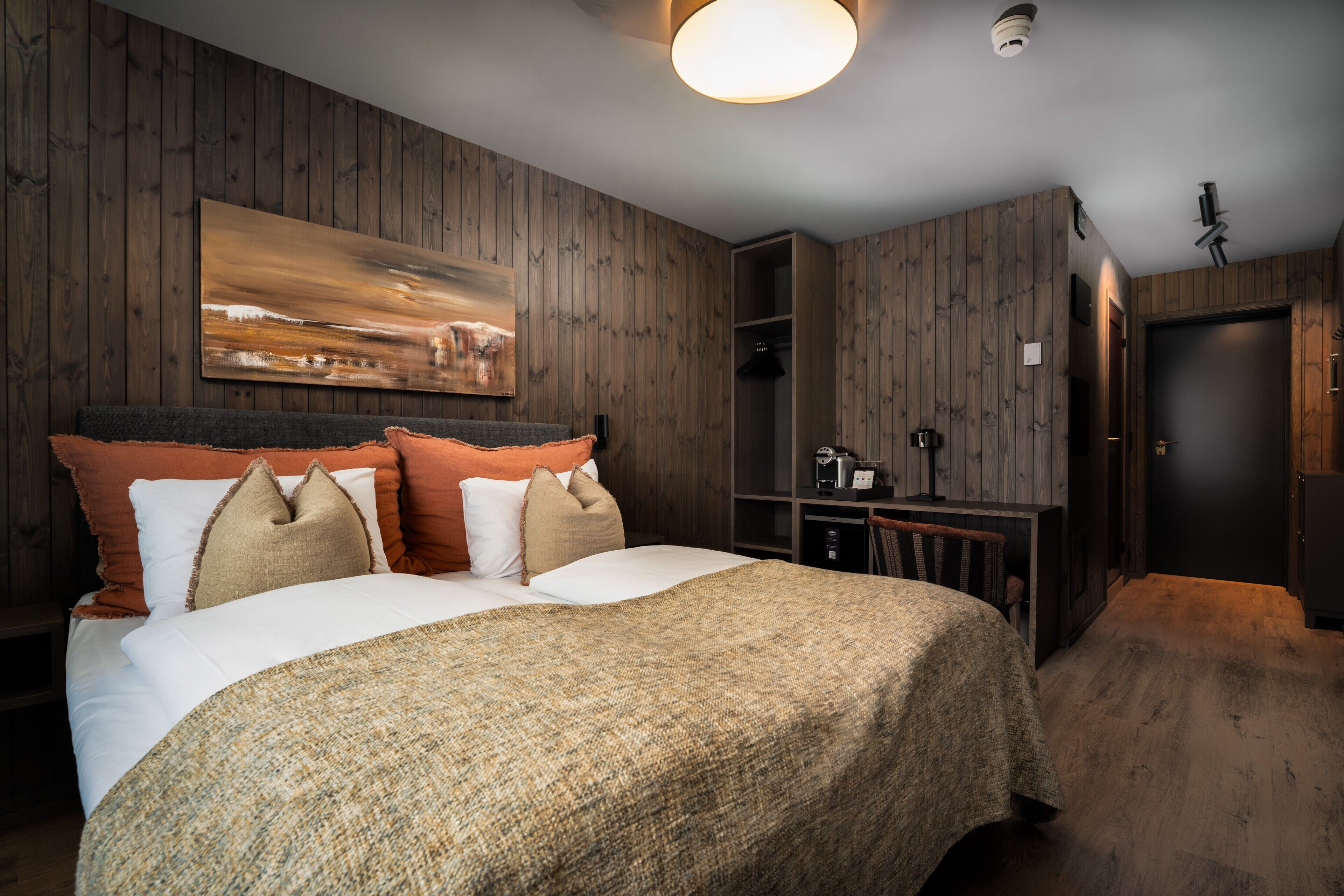 Une chambre à coucher avec un grand lit, des lambris en bois sur les murs, un tableau au-dessus du lit et une armoire.
