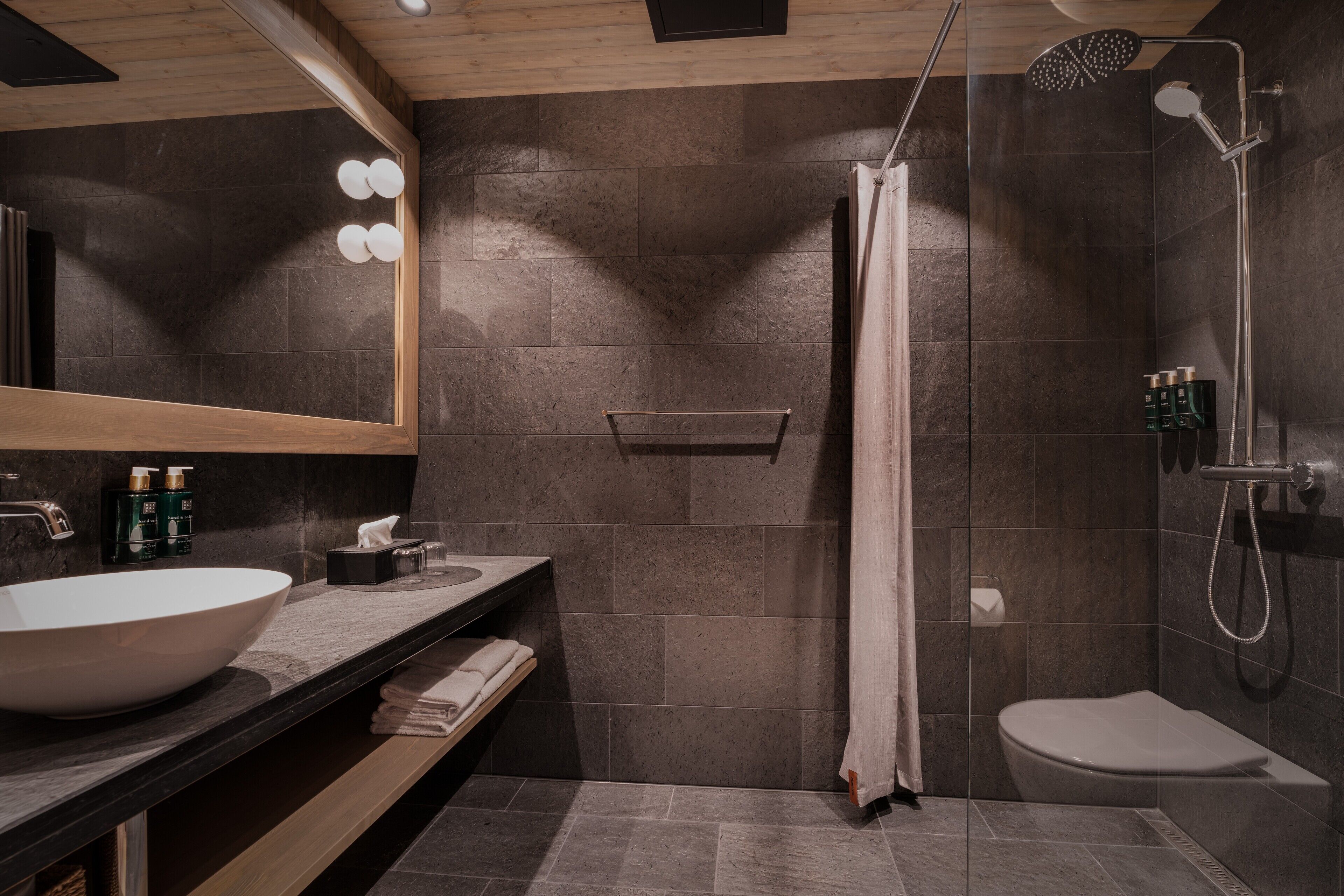 A modern bathroom with a large sink, a shower, and a toilet.