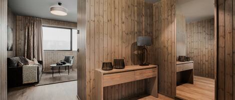 A modern room with wooden panel walls, a wooden console table with a lamp, a large mirror, a sofa, and a small table with chairs.
