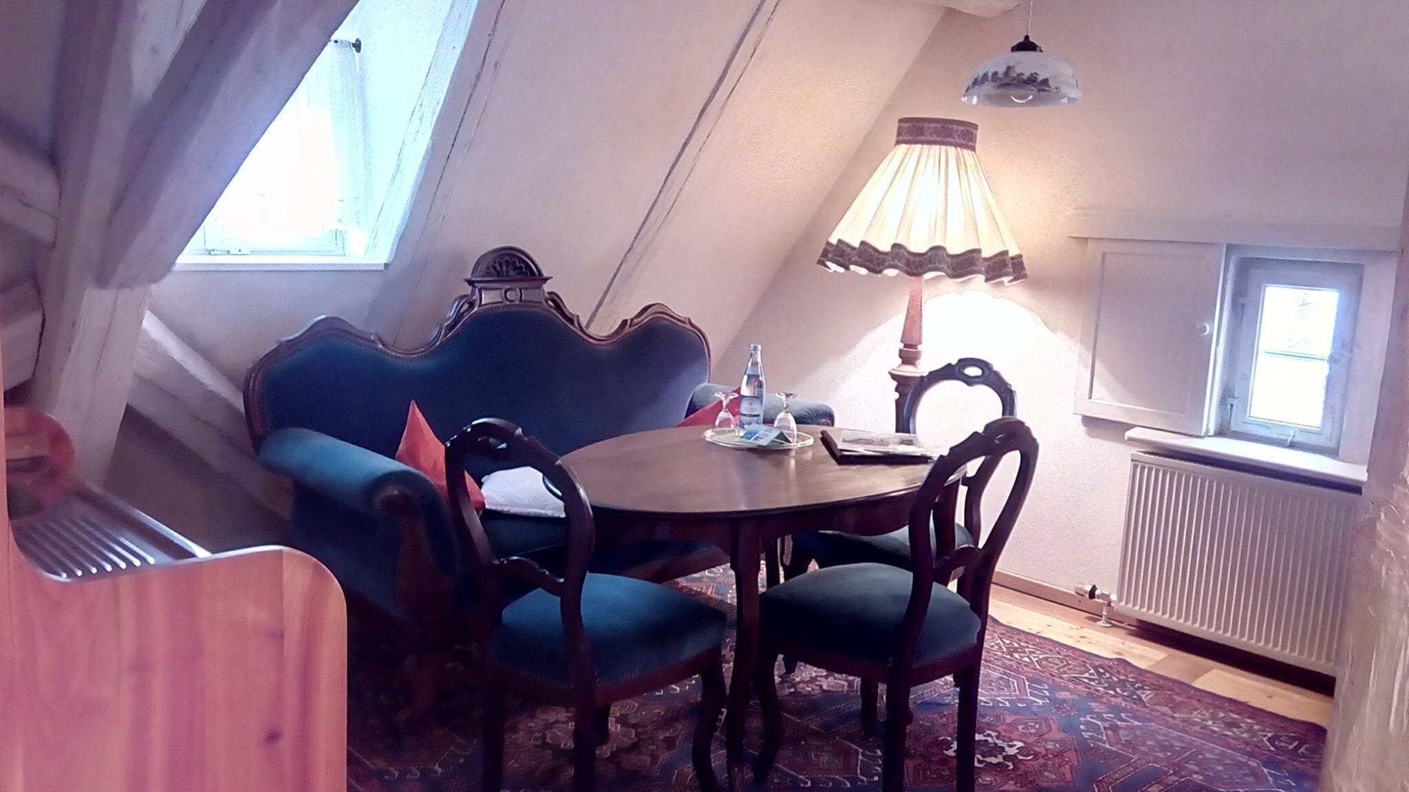 A cozy room with a round table, two chairs, a blue sofa, a lamp, and a radiator.