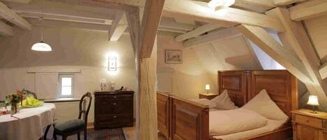 A bedroom with a wooden bed, a table with a chair, and a radiator.