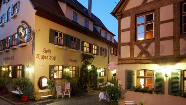 A traditional European courtyard with a restaurant named "Hotel Weisses Hof" and a small outdoor seating area with tables and chairs. - Hotel Weisses Ross (Dinkelsbuehl)