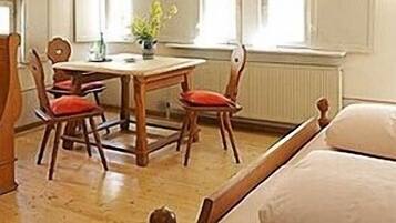 A cozy room with a wooden bed, a wooden chair, a small table, and a window with curtains.