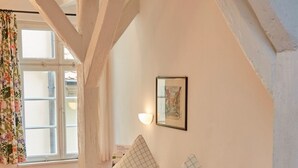 A bedroom with a wooden bed, a window with floral curtains, and a framed picture on the wall. - Hotel Weisses Ross (Dinkelsbuehl)