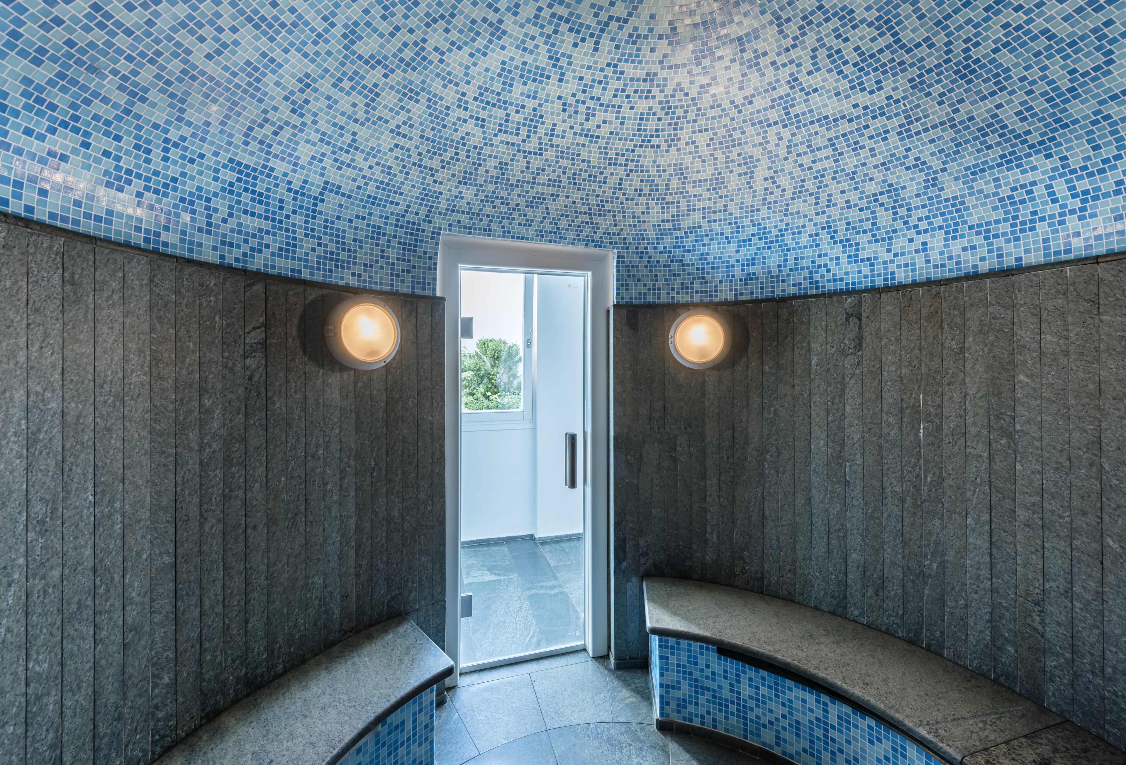 Ett spa-rum med ett kaklat tak, en dörr som leder ut och två bänkar.