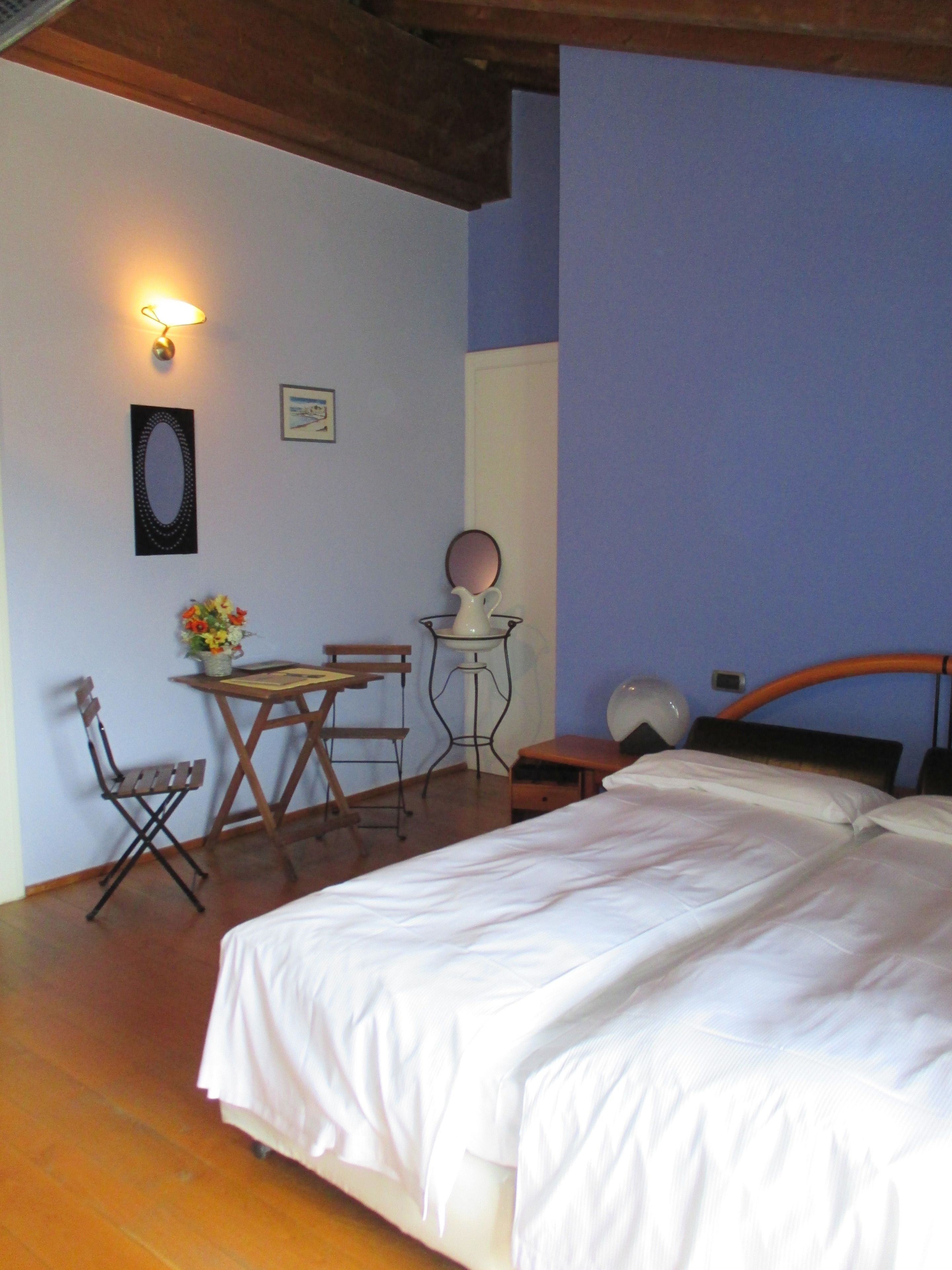 Une chambre à coucher comprenant un lit, une petite table avec des chaises, un miroir et un luminaire fixé au mur.