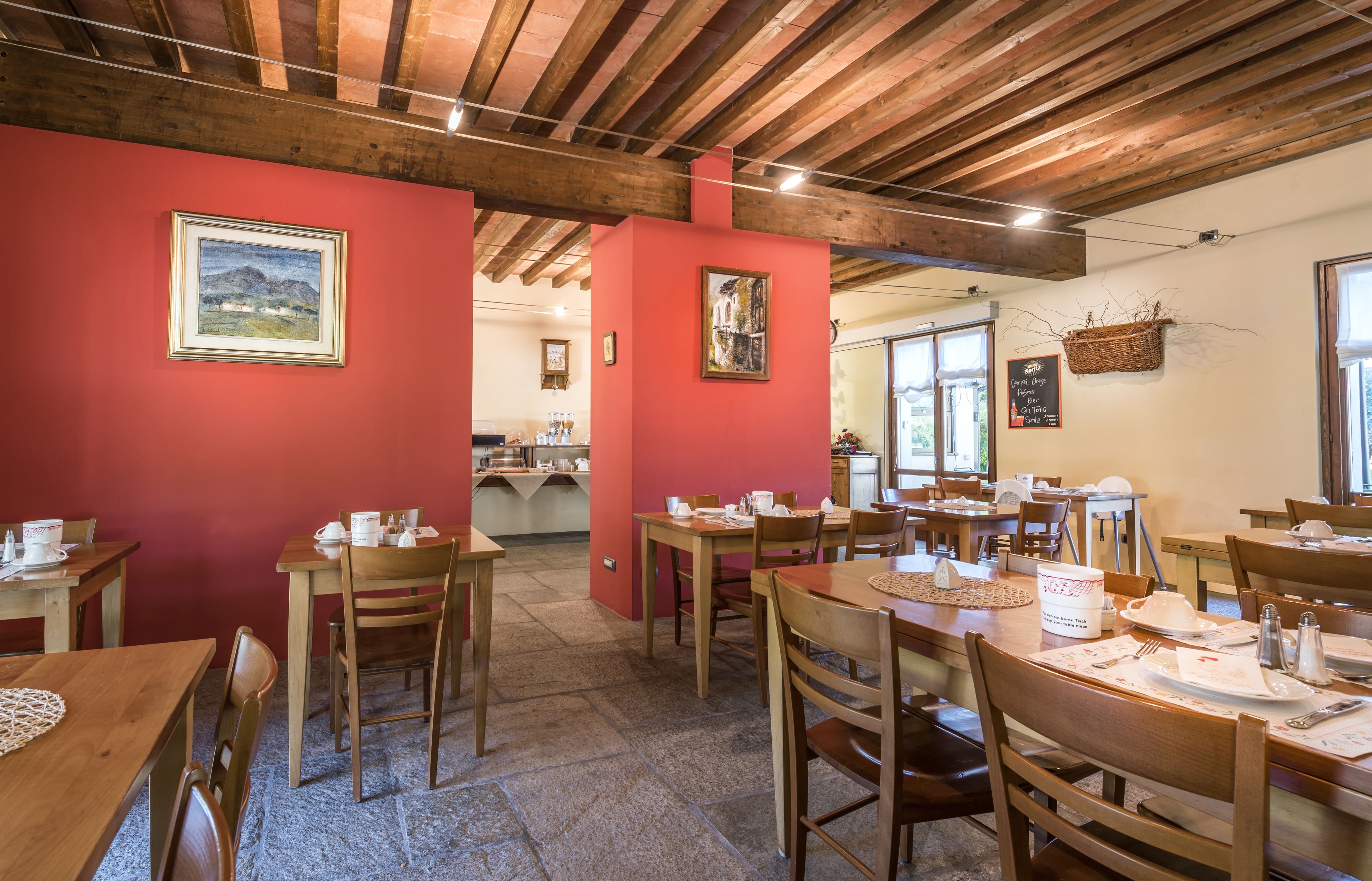 Un espace repas avec des tables et des chaises en bois, des murs rouges et des tableaux encadrés.
